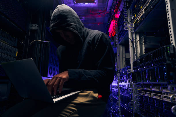 A photo of a hooded man in a server room with a laptop